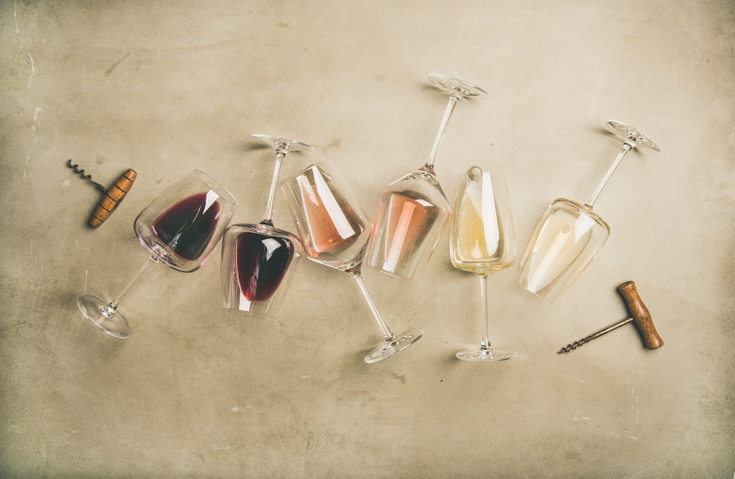 Rotwein, Rosé und Weisswein in liegenden Gläsern auf Beton, daneben zwei alte Korkenzieher